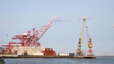 Lizbon, Portekiz 3 Haziran 2025: Tagus (Tejo) Nehrindeki Alcantara limanında açık mavi gökyüzünün altında kablolar ve istiflenmiş kargo konteynerleri bulunan sanayi turnaları.