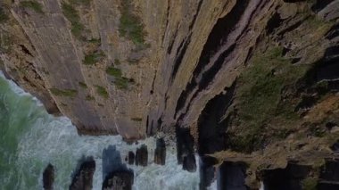 Aerial drone view above a dramatic cliff edge, revealing the crashing waves, churning ocean and jagged rocks far below. Powerful, cinematic scene over the seashore and abyss over the ocean. 