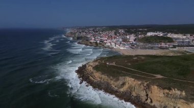 Dramatik uçurumlar ve geniş bir kumsal boyunca uzanan büyüleyici bir sahil kasabasının hava manzarası. Okyanus dalgaları berrak bir mavi gökyüzünün altında süzülüyor, güney kıyılarındaki bir köyde yazın güzelliğini yakalıyor..