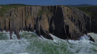 Dramatik kıyı manzarası, engebeli kaya oluşumları boyunca insansız hava aracı uçakları. Atlantik Okyanusu 'nun yeşil dalgaları yüksek dokulu kıyı şeridine çarpar ve güçlü bir deniz manzarası yaratır. Portekiz. 