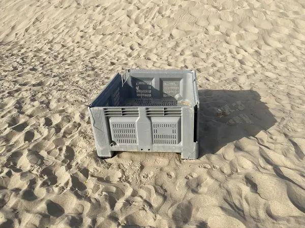 Kumsalda terk edilmiş gri balık plastik sandığı. Gölgeler, güneş. 