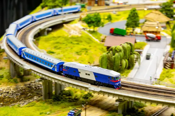 Mavi yolcu treni minyatür kırsal alanda yüksek raylarda seyahat ediyor.