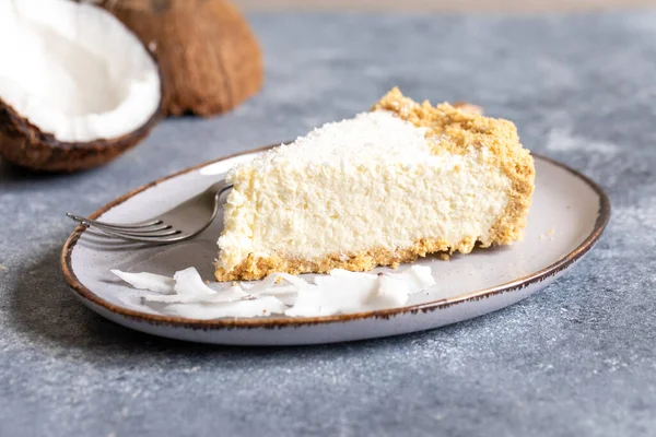 piece of coconut cheesecake on a plate with fresh coconut.