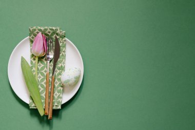 Yeşil masadaki lale yanında tabak ve peçete olan masa manzarası. Paskalya arkaplanı.