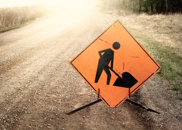 People working caution sign on rural dirt road with sun flare.