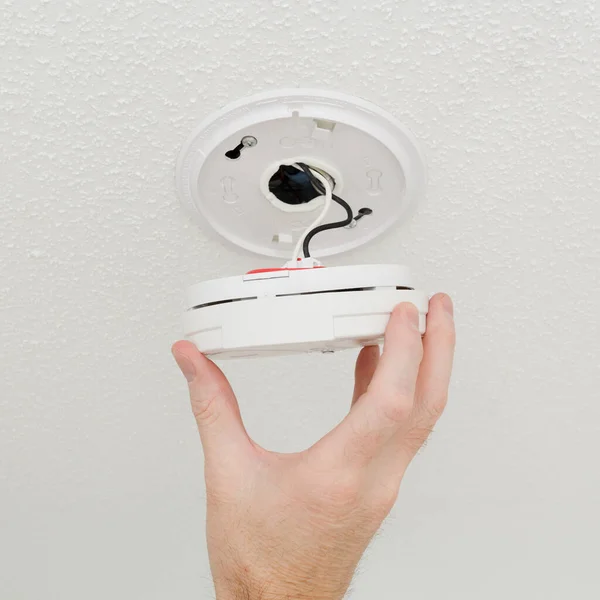 Stock image Person checking wired in ceiling smoke detector