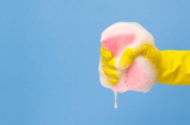 Rubber gloved hand holding soapy kitchen sponge with copy space