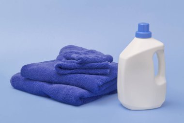 Çamaşır deterjanı şişesi ve havlular mavi üzerine.