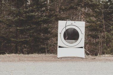 Kırsal bir yolun kenarında eski ve atılmış bir çamaşır kurutma makinesi.