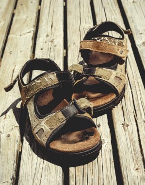 Güneşli bir günde tahta güvertede dinlenen bir çift sandalet.