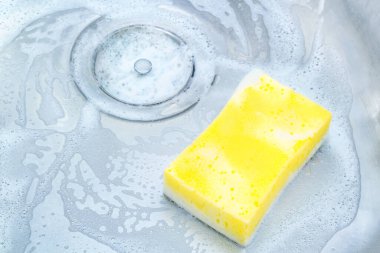 Mutfak lavabosu sarı bir süngerle temizleniyor.