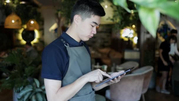 在通过便携式平板电脑在网上下订单之前 咖啡店认真的员工都穿着深绿色的围裙 穿着制服的有吸引力的餐厅经理通过互联网向送货部门传送网上定单 — 图库视频影像