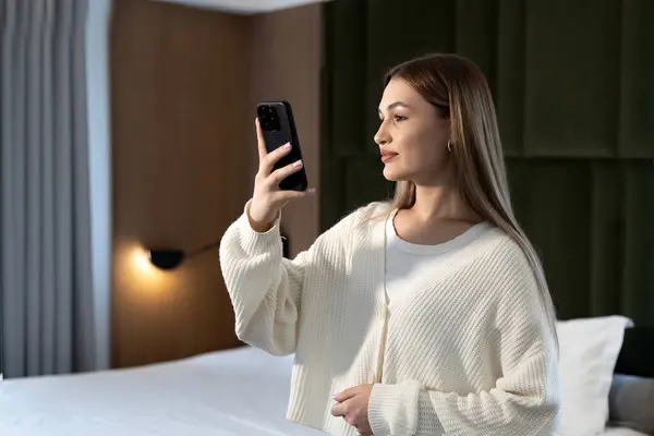 Genç Avrupalı bir kadın lüks bir otele geldikten sonra telefonuyla selfie çekiyor.