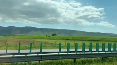 Güneşli bir günde yeşil tarlalardan ve dağlardan geçen arabanın yolcu penceresinden bir bakış açısı