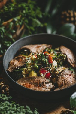 Siyah bir tavada brokoli, domates ve kabak gibi sebzelerle dilimlenmiş sağlıklı yiyeceklerin yakın plan görüntüsü. Domatesli biftek salatası ve siyah tavada salatalık. Yüksek