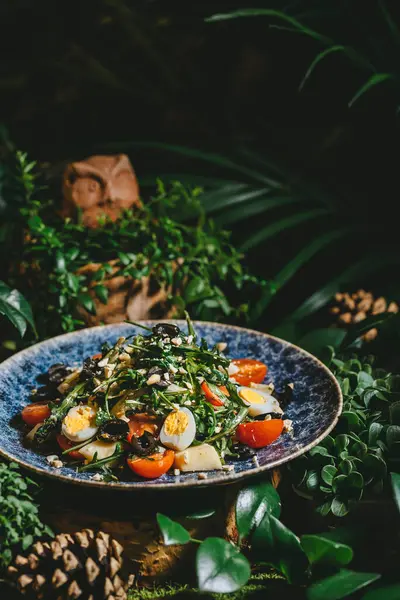 Mavi bir tabakta, kiraz domatesli, yumurtalı ve zeytinli, yemyeşil yapraklı taze bir salata. Mavi tabakta servis edilen kiraz domatesli, yumurtalı ve zeytinli salata.