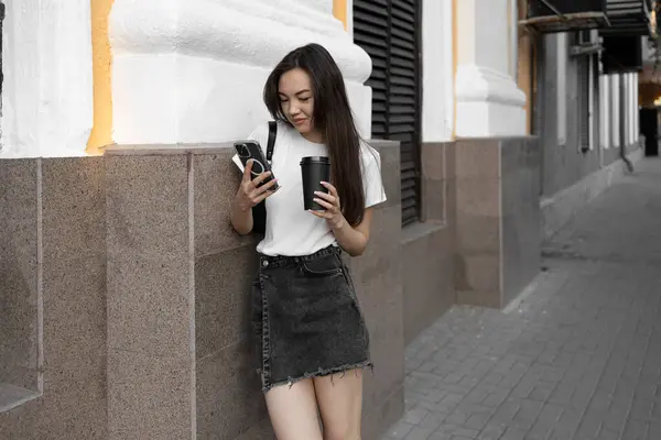 Beyaz t-shirt ve kot etekli sıradan bir genç kadın şehrin bir sokağında bir binaya yaslanmış elinde kahve fincanıyla akıllı telefonuna bakıyordu..