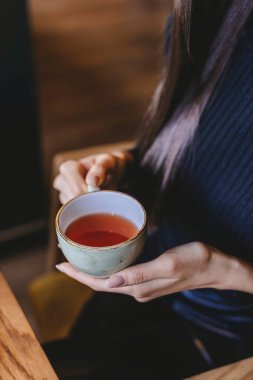 Şık, uzun saçlı esmer hoş bir kafede sıcak bir fincan çayın tadını çıkarıyor, güneş ışığı içeri akıyor. Ortam davetkar ve huzurlu, rahatlamak için mükemmel..