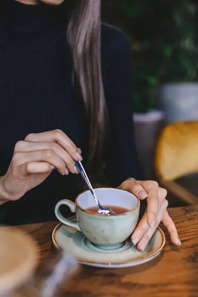 Yakından çekilen resimde siyah kazaklı güzel kızlar çayını yeşil bir fincanda karıştırıyor. Etrafı bitkilerle dolu sıcak bir kafe ile çevrili..