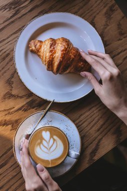 İsimsiz bir kadın bir fincan kahvenin tadını çıkarıyor. Yanında da altın, pullu bir kruvasan. Samimi bir kafe. Kahvaltı keyfi için sıcak bir ortam. Düz yatıyordu