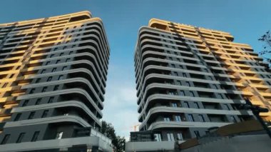 Şık modern yerleşim kuleleri güzel bir gökyüzüne karşı yükseliyor, eşsiz mimari tasarımlar sergiliyor ve şehir manzarasında sıcak bir akşam parlıyor..
