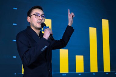 İş konferansı sırasında veri eğilimlerini büyük ekranda sunan akıllı ortak büyümeyi gösteren bir bar tablosuna işaret ediyor. İş adamı toplantı odasında konuşma yapıyor..