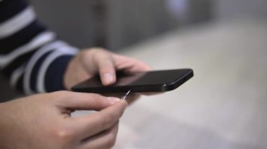 Tanımlanamayan kişi akıllı telefondan SIM kartı çıkarıyor. Erkek eli cep telefonundan SIM kart yuvasını fırlatıyor. Mobil uzmanlar metal püskürtücü kullanan bir cihaz kullanıyor..