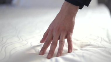 Bilinmeyen el, yumuşaklığını ve rahatlığını gösteren peluş, beyaz bir yatağa dikkatlice bastırır. Kimliği belirsiz şahsın pansiyon takımlı el yapımı yatağı..