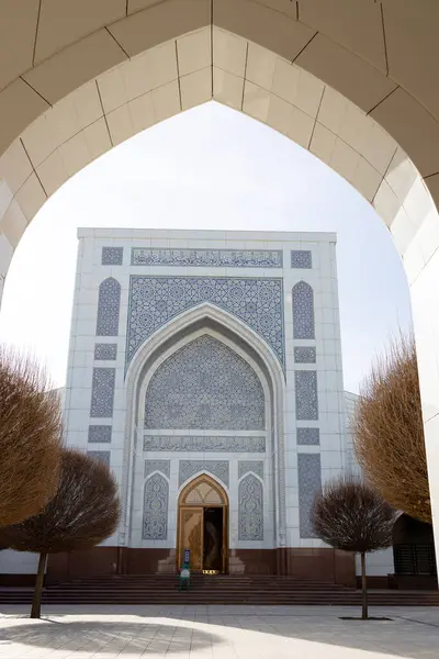 Taşkent, Özbekistan - 25 Ocak 2025: Şık desenler, iki büyük kemerle çerçevelenmiş ve simetrik ağaçlarla kaplanmış çarpıcı bir Küçük Cami 'nin cephesini süslüyor.