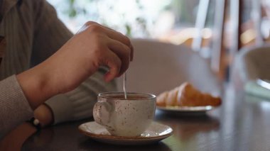 Kafede kahvaltı, bir fincan americano kahvesi ve taze pişmiş hamur işi ile yerel restoranın ahşap masasında geniş pencereli güneş ışığı ile. Kafede arkadaşını bekleyen ve sıcak bir şeyler içen bir adam..