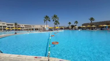 Sharm El Sheikh, Mısır - 13 Mart 2025: Ziyaretçiler palmiye ağaçlarıyla çevrili turkuaz su havuzuyla güneşli bir öğleden sonra geçiriyorlar..