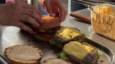 Eller ağız sulandırıcı burgerleri ızgara köfteler, taze marul, domates dilimleri ve erimiş peynirle ustalıkla birleştirir. Açık hava pikniğinin canlı atmosferinin tadını çıkar..