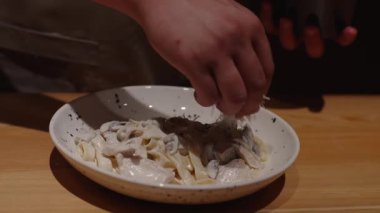 Şef sotelenmiş mantarlı krema sosuyla kaplı lezzetli bir tabak fettuccine hazırlıyor. Makarnayı peynirle dekore et. Güzel yemek konsepti.