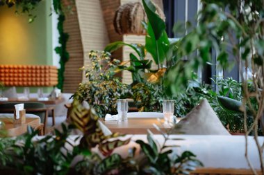 Modern yemek alanında verimli yeşilliklerle çevrili zarif mobilyalar bulunur. Masalı güzel bir lokanta, bardaklar ve çatal bıçaklarla dolu..