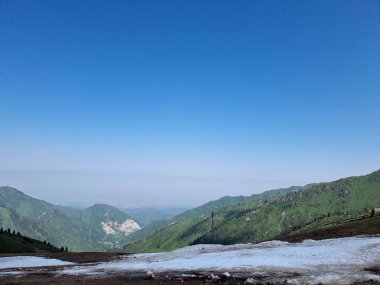 Dağlarda yaz günü. Erimemiş karın kalıntıları dağların tepelerinde yatıyor. Dağ sıraları bitki örtüsüyle kaplı