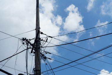 Messy and tangled electrical power lines on a utility pole against a blue sky