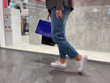 Alışveriş merkezinde el çantalarını tutan tanınmamış bir kadın. Alışveriş merkezinde kadın bacakları kapalı ve kapalı alanlarda dolaşır. Mal ve hediye almak, alıcı konsepti.