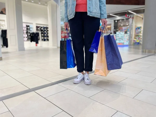 Alışveriş merkezinin ortasında elinde bir sürü alışveriş çantası taşıyan tanınmamış bir kadın. Alışveriş merkezindeki kadın bacaklarını alışverişlerle kapat. Alışverişkolik alıcı, satış kavramı