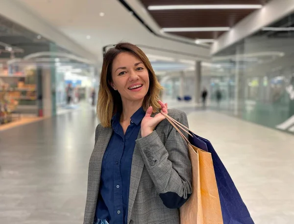 Mutlu yüzlü, orta yaşlı beyaz bir kadın alışveriş merkezinde kameraya bakıp gülümsüyor. Güzel, mutlu, kağıt torbalı, alışverişten sonra mutlu bir kadın. Pozitif duygular