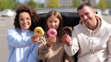 Kameralar mutlu beyaz aile babalarından ve genç kızlarından el ele tutuşmuş kameralara gülümsüyor. Genç kızlı çift arabanın bagajında donut gösteriyor.