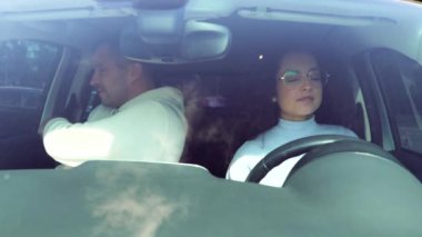 Beyaz tenli yakışıklı erkek sürücü eğitmeni arabada yolcu koltuğunda oturuyor ve sürücü kursunda bayan öğrenciye yol gösteriyor. Güzel, çekici, genç bir kadın araba kullanıyor. Ehliyet sınavı