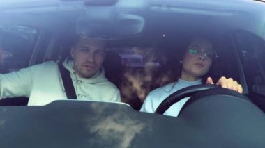 Güzel genç bir bayanın araba kullanmasına ve sürücü kursunda kız öğrenciye yol göstermesine yakın. Genç ve güzel bir bayan acemi erkek yolcu koltuğunda otururken araba sürüyor.