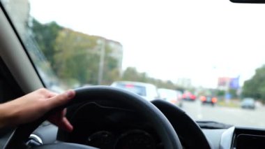 Adam elleri direksiyonda. Kapatın. 4K video. Yolda araba süren bir erkek. Arka planda birçok araba var. Yolculuk, yolculuk. Şehir yaşam tarzı. Otomobil sürüyorum. Sürücü arabada. Trafik kavramı