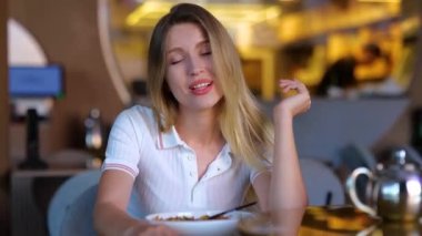 Beautiful joyful young female sitting in restaurant and talking to camera. Close up of happy pretty woman on a date in bar speaking and looking at camera in positive mood and smiling. Cafe concept