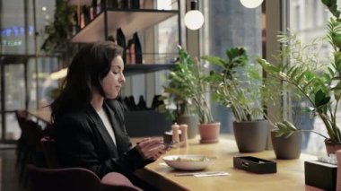 Genç, beyaz, güzel, siyah, uzun saçlı ve hoş bir gülümsemesi olan bir kadın. Çağdaş bir restoranda, ahşap bir masada oturuyor. Kız salata yiyor, yemeğinin tadını çıkarıyor ve telefonda konuşuyor..