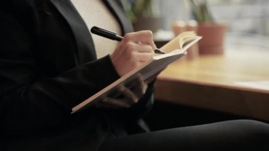 Siyah ceketli, beyaz bluzlu, uzun kahverengi saçlı, güzel ve zeki beyaz bir kadın restoranda oturmuş, defterini çiziyor ve dışarıdaki büyük pencereden bakıyor..