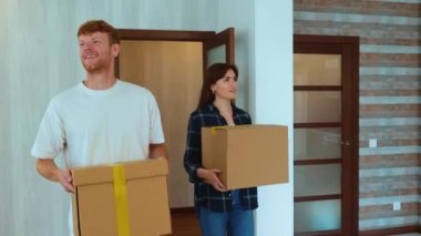 Portrait of Caucasian cheerful young couple in good mood entering their new apartment holding boxes in hands and putting them down on the floor. Moving in together, relocation. Family home. Marriage