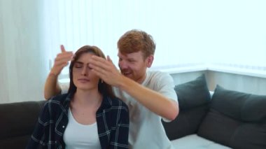 Camera moving back from young happy couple sitting on sofa in new apartment with many boxes. Relocation concept. Moving in together. Marriage mortgage. Husband surprised his beloved wife in new home