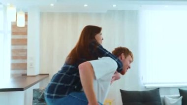 Close up of cheerful Caucasian man and woman having fun playing in new house on moving day. Piggyback ride. Happy young family couple in home with many boxes moving in together. New home concept. Real