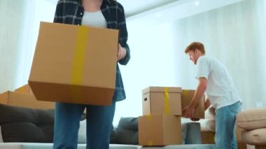 Close up of joyful positive young man and woman indoors in room with many boxes putting stuff on floor. Married couple with cardboard boxes in new apartment. Relocation. Moving day. Real time
